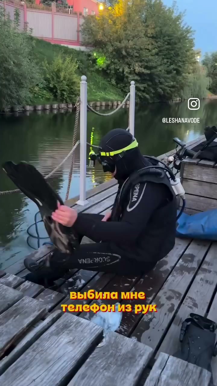 Водолаз в гидрокостюме на деревянном настиле набережной достаёт телефон из реки Упы