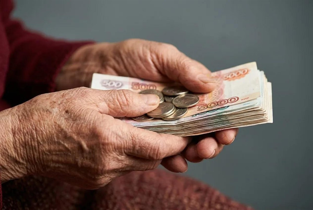 Пожилые руки держат рублёвые купюры и монеты